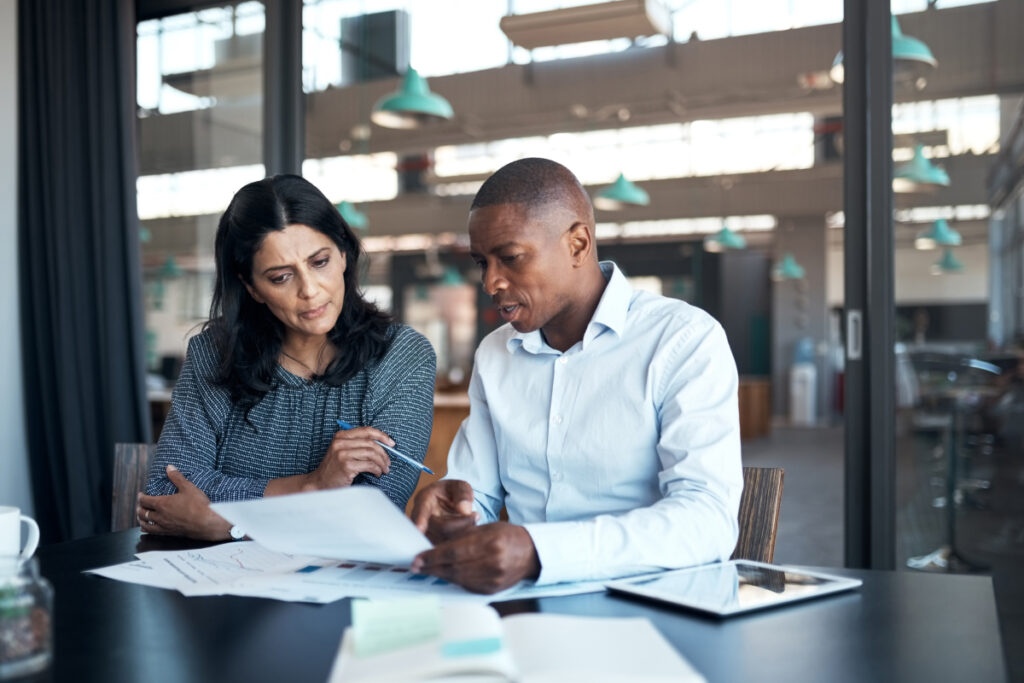 Two business professionals reviewing documents and data reports together at an office desk