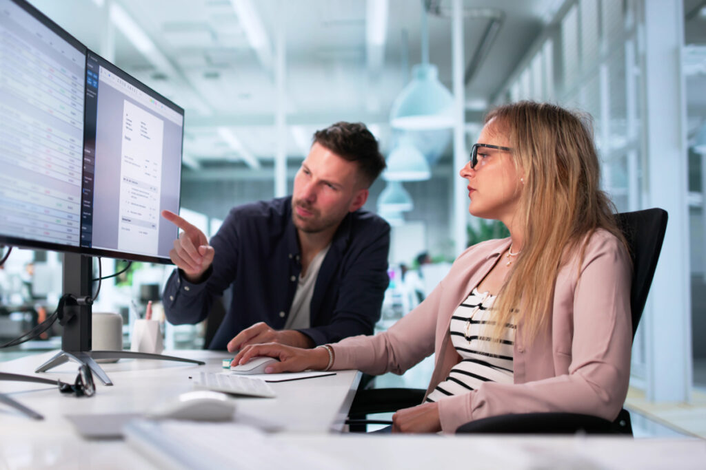 Business team reviewing data dashboards on dual monitors during an office meeting