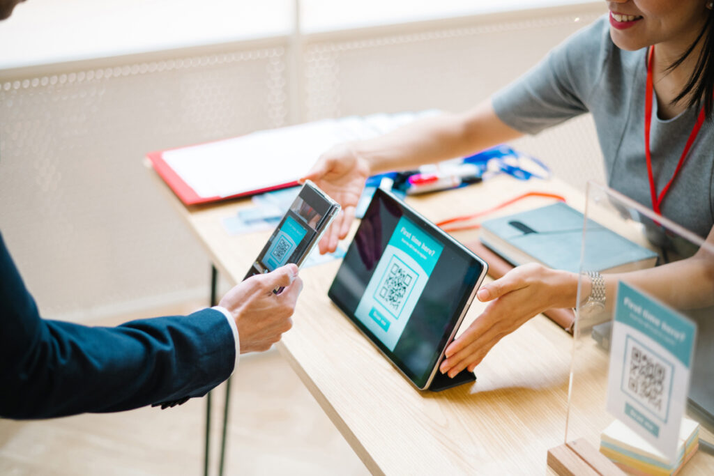 Receptionist and visitor scanning a QR code on a tablet at a front desk check-in