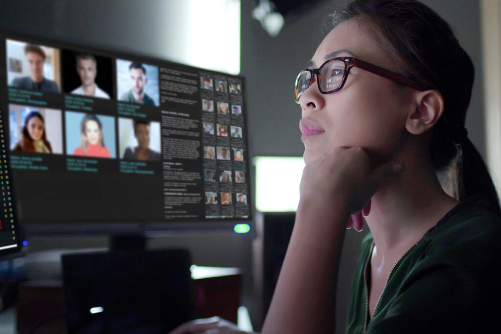 Woman wearing glasses studying a facial recognition or identity verification database on a monitor in a dimly lit office